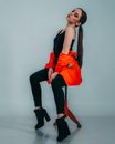 Side view full length photogenic young professional female model wearing trendy clothes sitting gracefully on high bar stool in studio during photo session