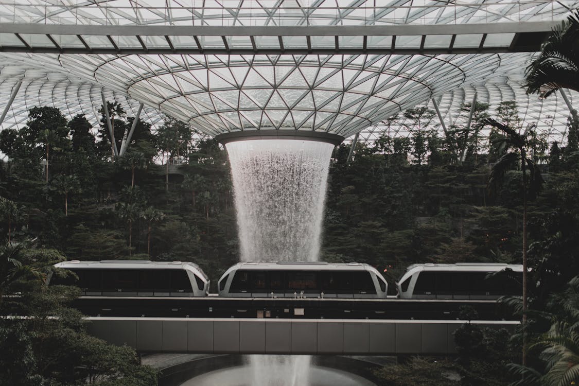 Free Contemporary rail link train going under indoors waterfall streaming from creative glass ceiling in Jewel Changi Airport in Singapore Stock Photo