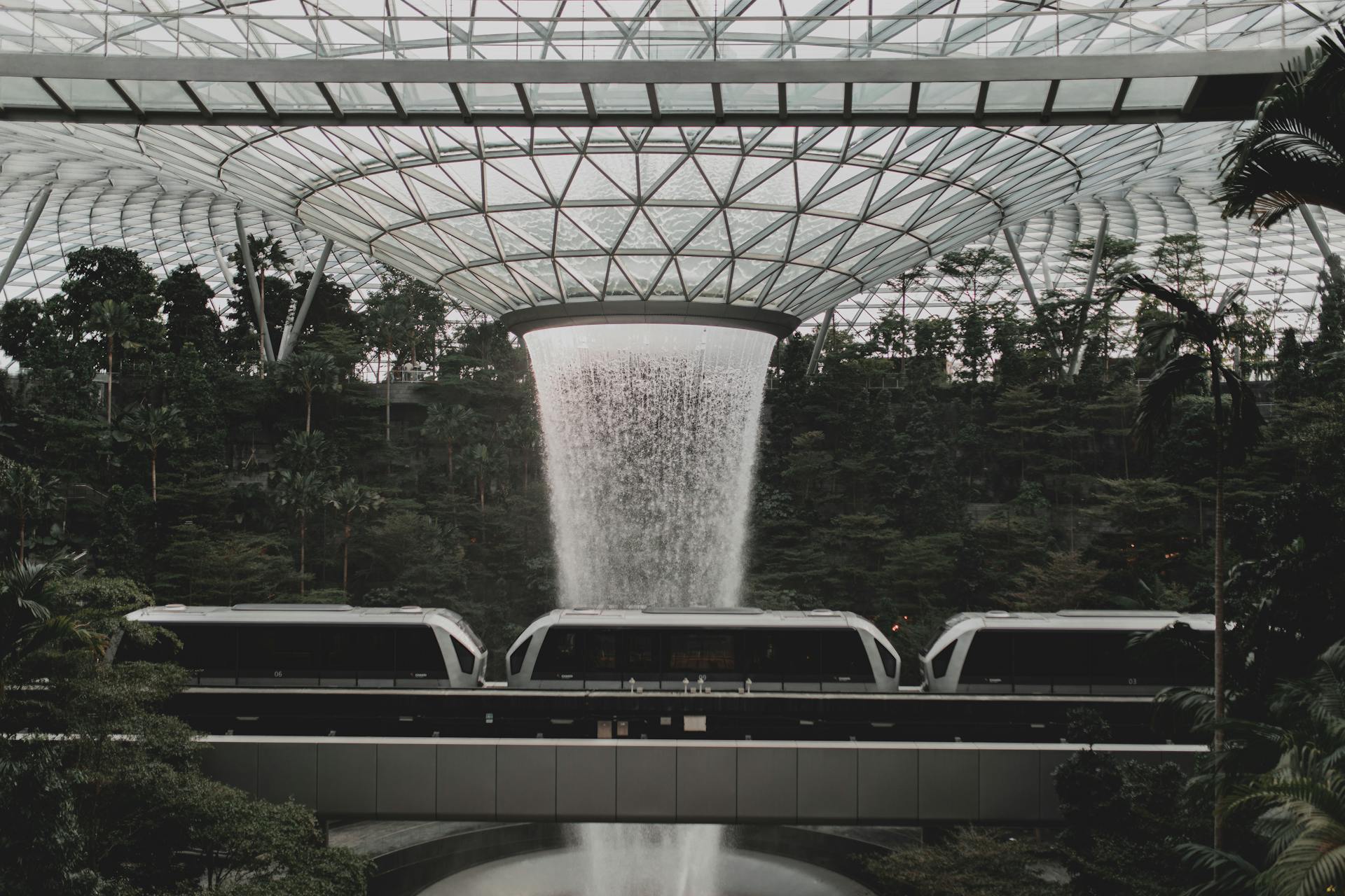 Contemporary rail link train going under indoors waterfall streaming from creative glass ceiling in Jewel Changi Airport in Singapore