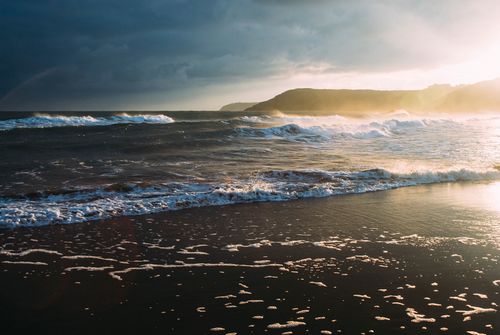 Free Captivating waves on a sandy beach during sunset, with a dramatic sky. Stock Photo