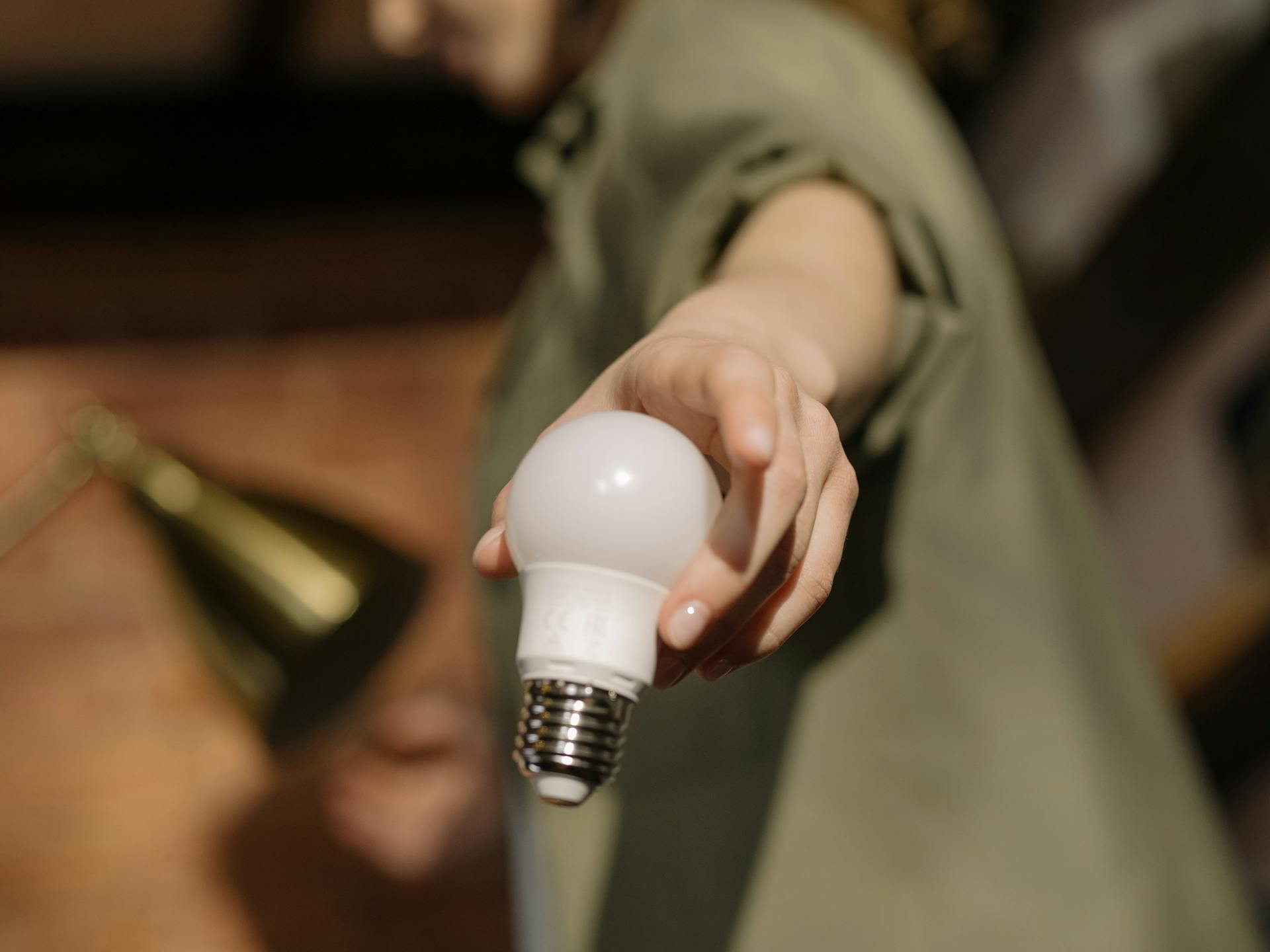 Close-up of a hand holding an LED light bulb indoors, symbolizing energy efficiency and modern home living.