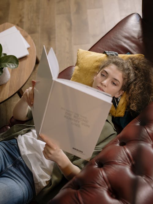 Woman Reading Book while Lyding Down on a Sofa 
