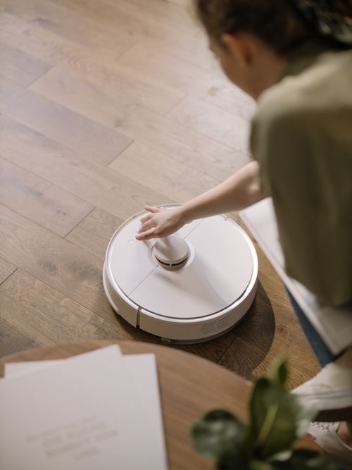 Free A woman interacts with a robotic vacuum on a wooden floor, showcasing smart home technology. Stock Photo