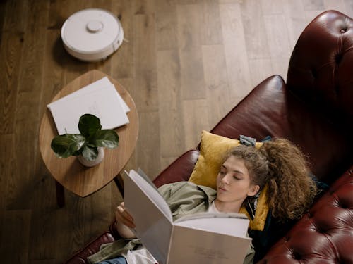 Free Woman Reading Book while Lyding Down on a Sofa  Stock Photo