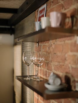 A warm kitchen scene with shelves, glassware, and a rustic brick wall.