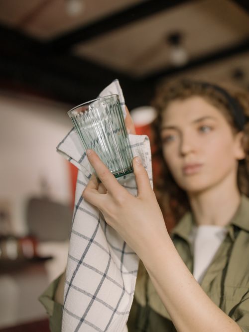 Free A young woman with curly hair dries a glass at home, focusing on cleanliness and domestic care. Stock Photo