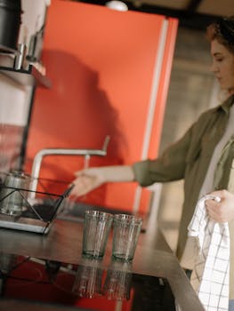 A young woman in a modern kitchen drying dishes with a towel by a bright red fridge.