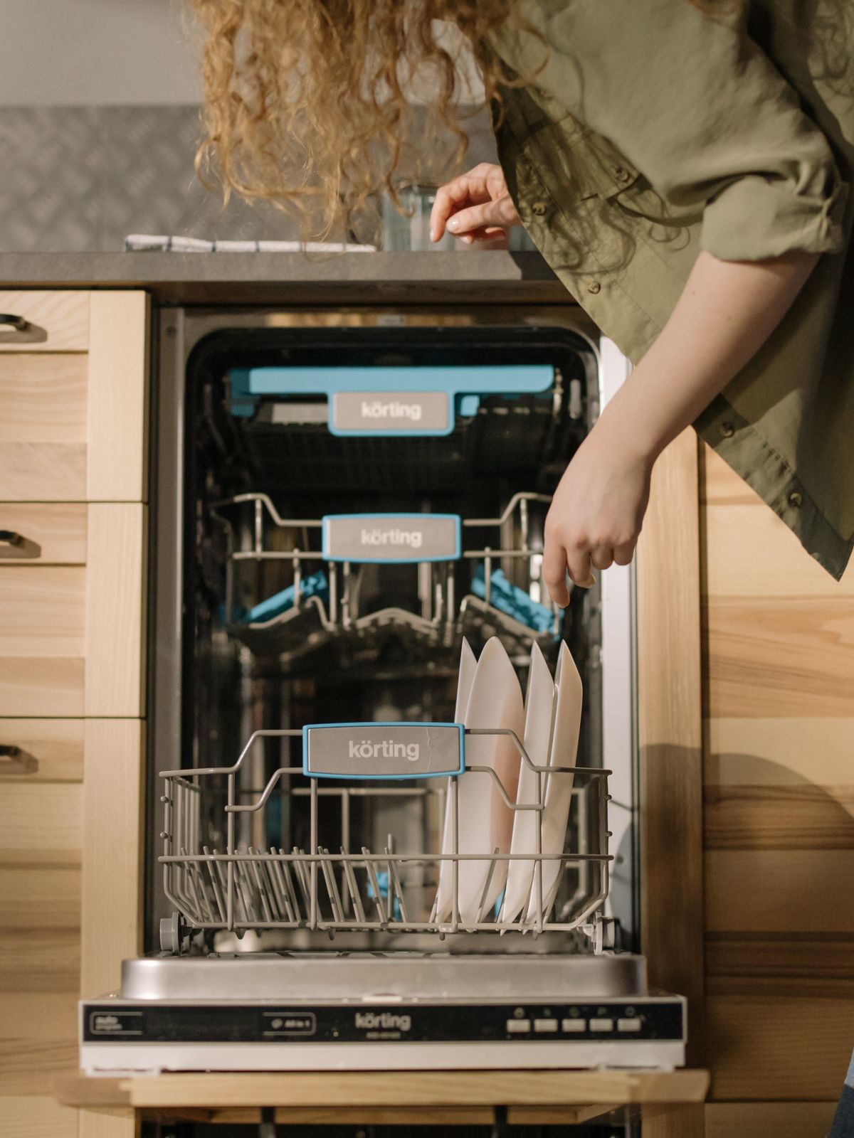 hands placing plates into an open dishwasher, demonstrating proper dish loading