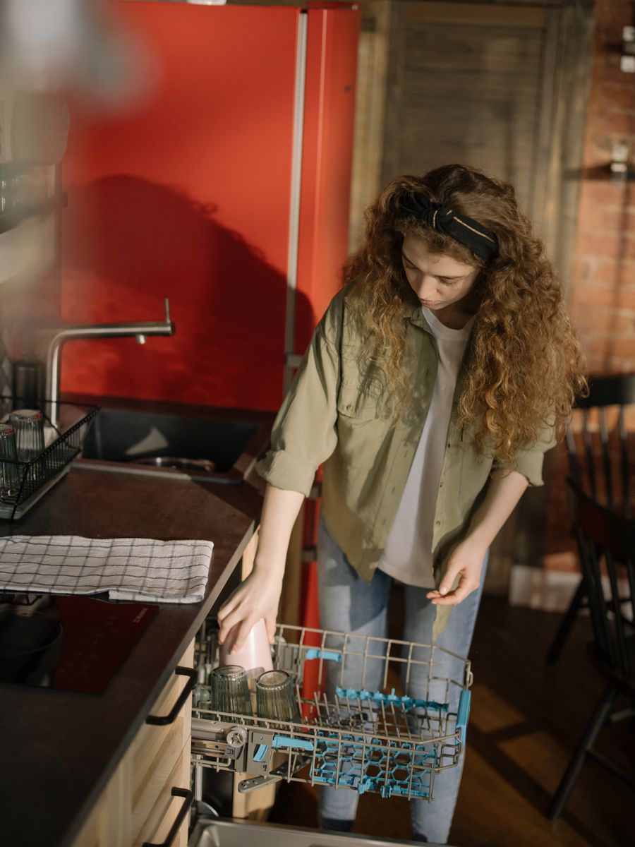 A woman loading the lower rack of a dishwasher in a kitchen with a red wall