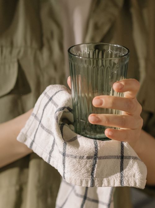 Free Close-up of a hand drying a green glass tumbler with a checkered dish towel at home. Stock Photo