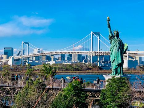 Replica of Statue of Liberty located in Tokyo against modern Rainbow Bridge and contemporary metropolis cityscape on clear sunny day