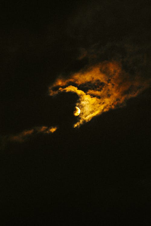 From below of bright full moon shining through thick clouds in dark night sky