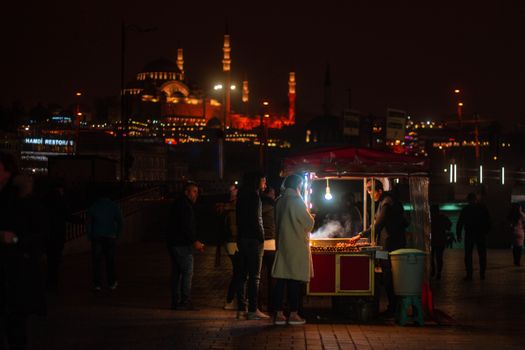 City night scene with locals enjoying street food in İstanbul, featuring illuminated mosques.