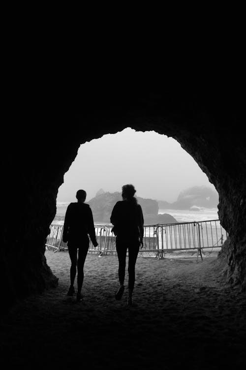 Silhouettes of anonymous women walking along rocky tunnel at seaside