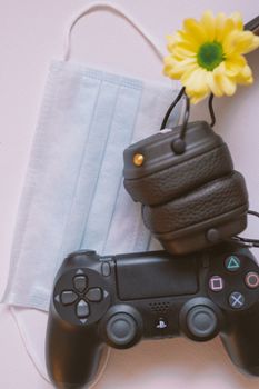 Close-up of gaming controller, headphones, mask, and flower on a flat surface.