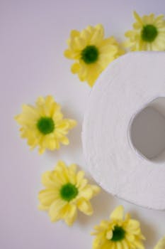 Yellow flowers arranged around a toilet paper roll on a white surface, creating a floral composition.