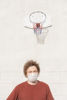 Portrait of a young man wearing a face mask under a basketball hoop, representing the new normal.