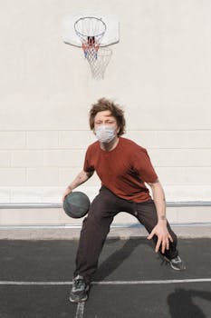 Man wearing a mask playing basketball on an outdoor court during the day.
