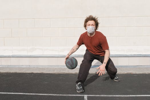 Man playing basketball outdoors while wearing a mask, illustrating sports during the pandemic.