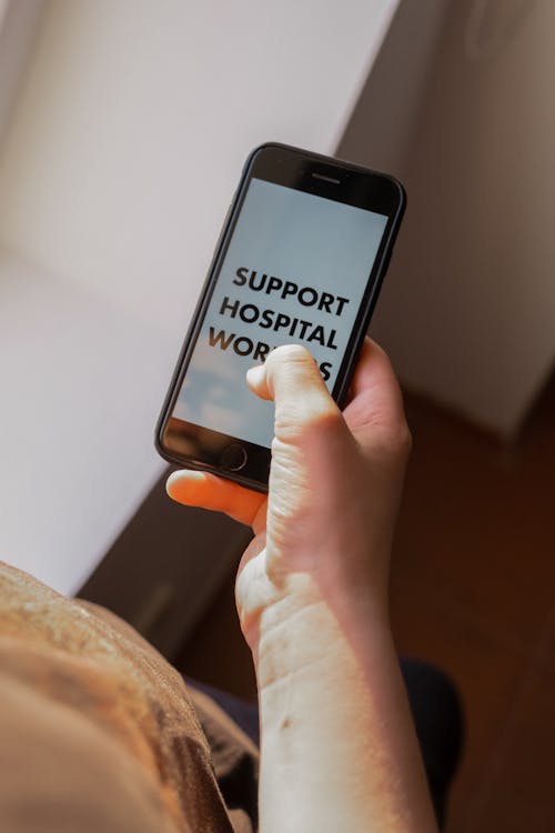 From above anonymous male in casual clothes showing smartphone with SUPPORT HOSPITAL WORKERS inscription illustrating social responsibility concept during coronavirus pandemic
