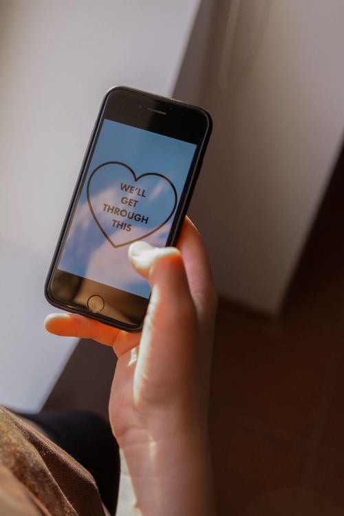 Free Hand holding smartphone displaying heart-shaped motivational message 'We'll Get Through This'. Stock Photo