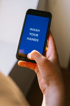 Close-up of a hand holding a smartphone displaying a 'Wash Your Hands' reminder on the screen.