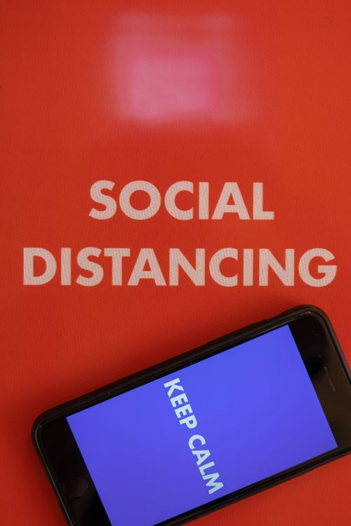 Free Vertical shot of a smartphone displaying 'Keep Calm' next to 'Social Distancing' text on a red background. Stock Photo