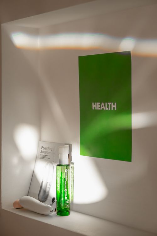 Free Vertical shot of cosmetics and a green 'Health' poster on a white shelf. Bright and minimalist. Stock Photo