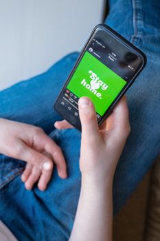 A person holding a smartphone displaying a green 'stay home' message while indoors.