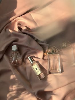Aesthetic still life of elegant perfume bottles on luxurious pink satin, beautifully lit.