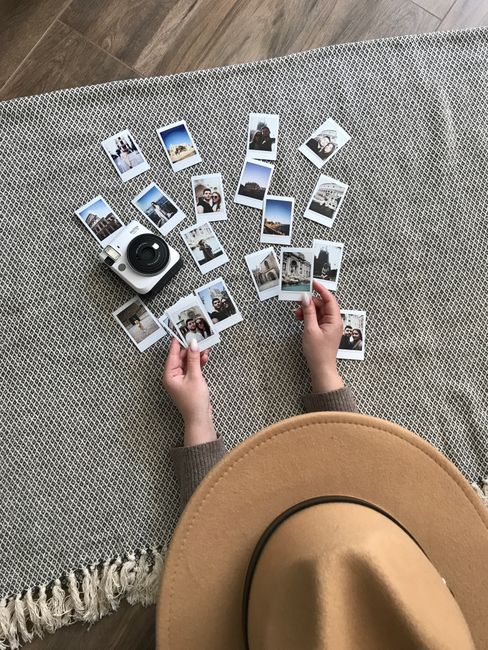 A flat lay image of instant photos arranged with a camera and hat on a textured surface.