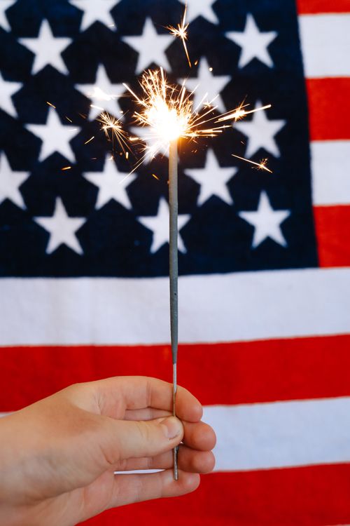 Free Close-up of a hand holding a sparkler in front of the American flag, symbolizing patriotism. Stock Photo