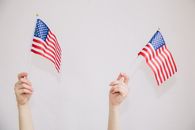 Crop anonymous female showing United States flags against white background illustrating national emblem with stars and stripes