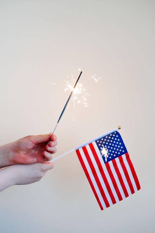 Free Close-up of hands holding a USA flag and sparkler, symbolizing celebration and patriotism. Stock Photo