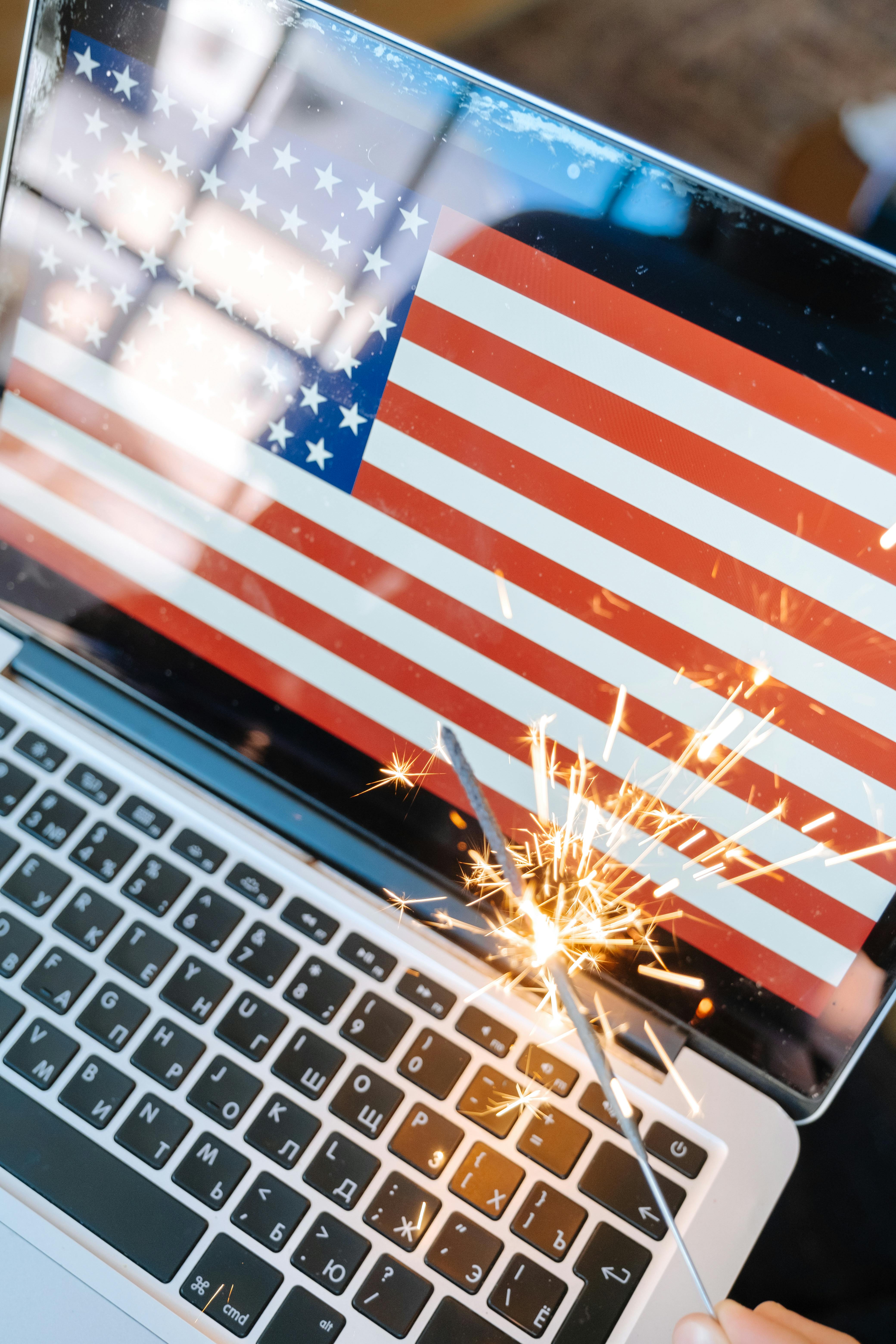 Laptop screen displaying USA flag with a sparkler for a festive, patriotic celebration.