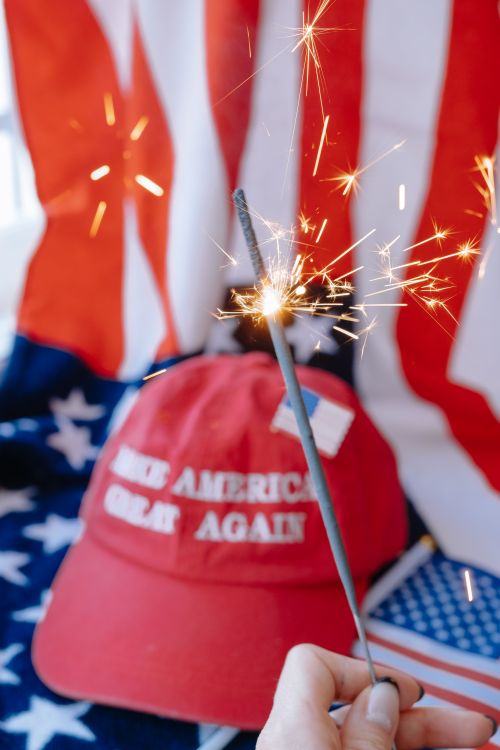 Free Close-up of a 'Make America Great Again' hat with a sparkler, American flags in the background. Stock Photo