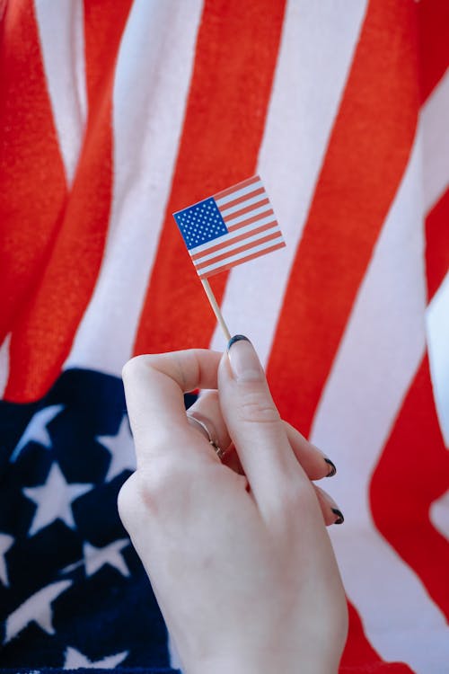 Woman Holding a Mini American Flag on the Background of a Big Flag