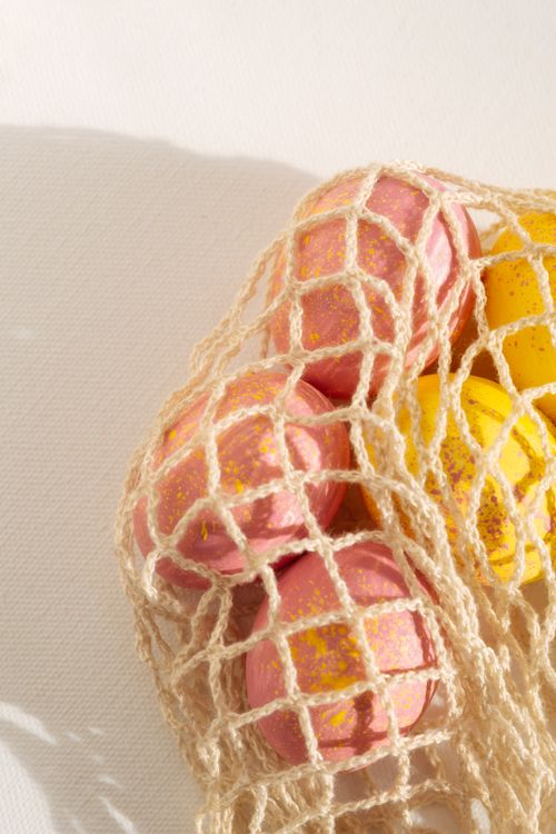 Free Pink and yellow Easter eggs captured in a net bag, perfect for Easter celebration themes. Stock Photo