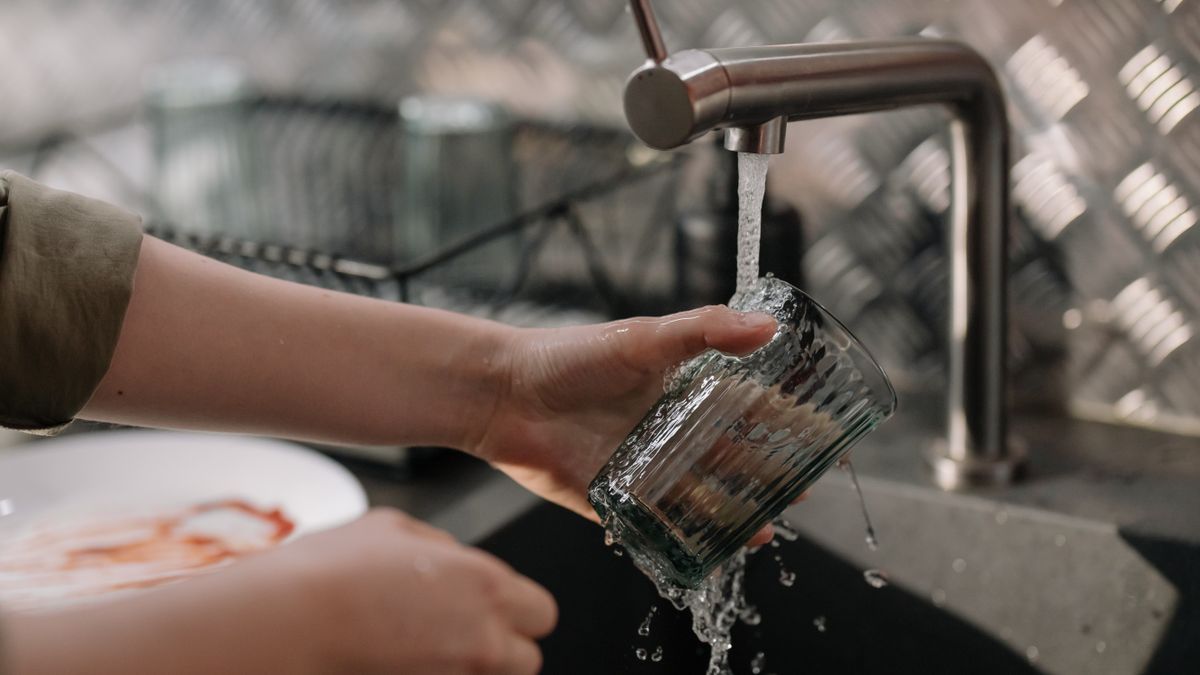 Nitrates in tap water being poured into a clear drinking glass under a kitchen faucet