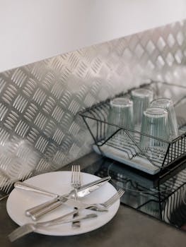 Clean and organized modern kitchen counter with stainless steel accents, showcasing dinnerware and glassware.