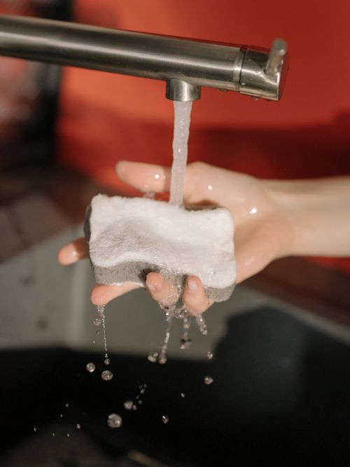 Free A detailed shot of a hand cleaning a sponge under running water from a tap. Stock Photo