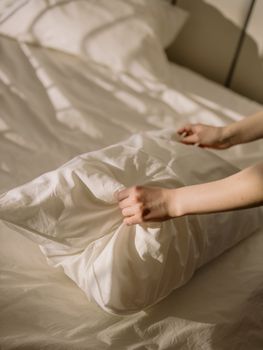 手在铺得整齐的床上调整枕头的特写，沐浴在温暖的阳光下