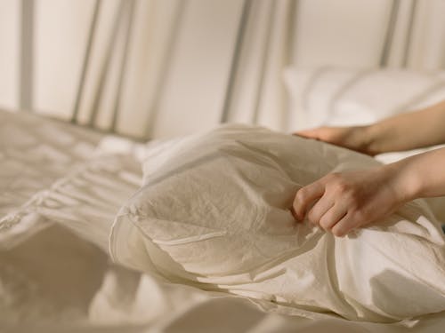 Person Holding White Textile on Bed