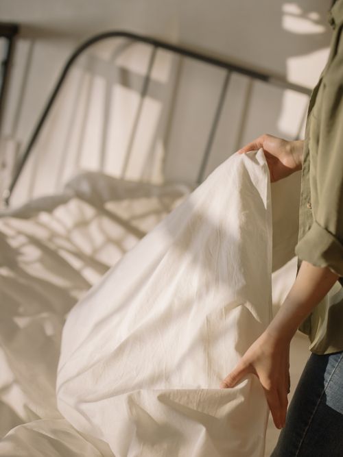 Free A person making a bed in a sunlit room, highlighting the comfort and tranquility of the space. Stock Photo