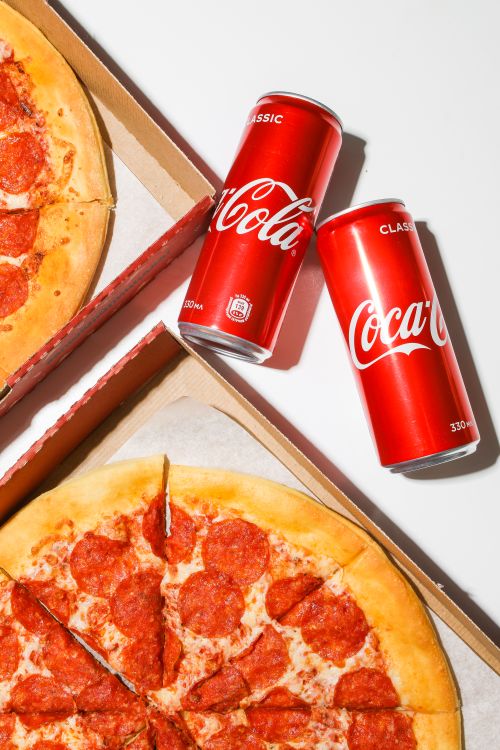 Free Aerial shot of pepperoni pizza with two cola cans in bright lighting. Stock Photo