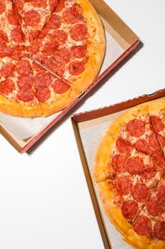 Top view of two pepperoni pizzas in cardboard boxes, ready to be served.