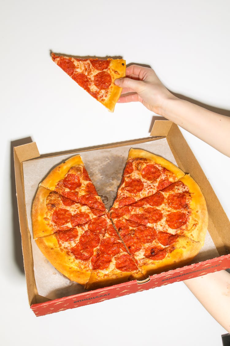 Person Holding A Slice Of Pizza