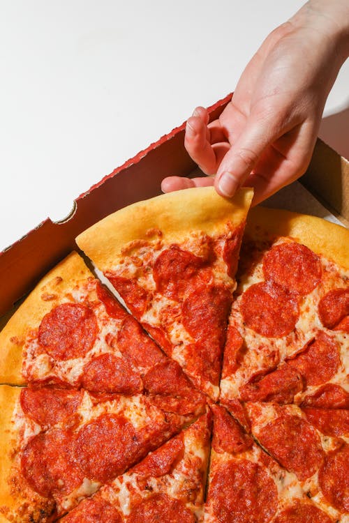 Person Holding A Slice Of Pizza