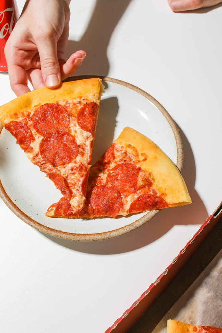 Person Holding A Slice Of Pizza On A Plate