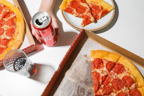 Free Person Holding Coca-Cola In Can Beside Pizza on Table Stock Photo
